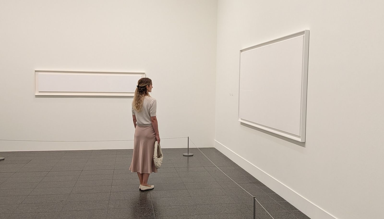 Eine Frau betrachtet in einem hellen Museumsraum großformatige weiße Bilder
